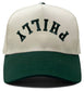 Adult Philly trucker hat with upside-down green lettering, beige front and green brim
